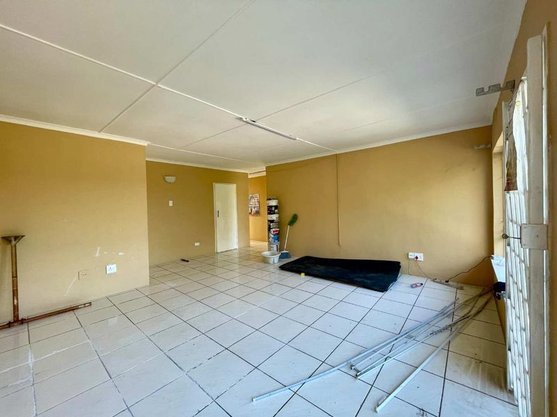 An empty living area featuring tiled flooring and a security gate, requiring cosmetic updates and repairs to the ceiling and floor finishes.