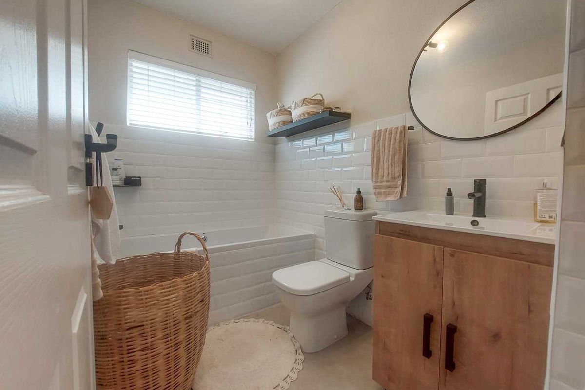 A modern bathroom featuring a built-in bathtub, subway tile wall cladding, a vanity cabinet with a basin, and a circular wall-mounted mirror.