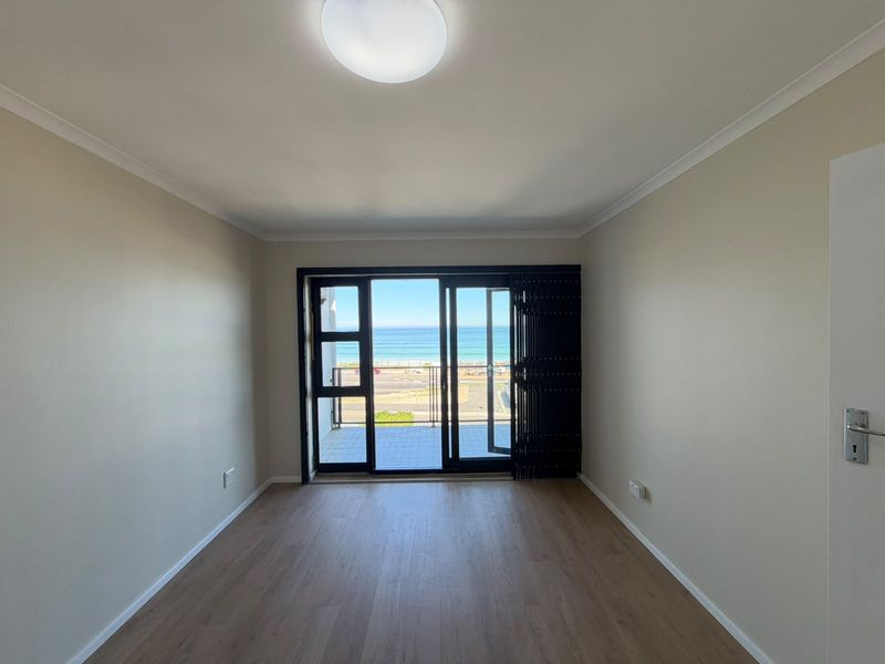 An empty, well-maintained living room featuring modern laminate flooring and large sliding glass doors that open onto a balcony with ocean views.