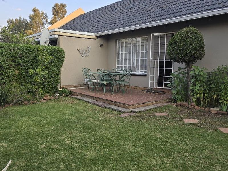 Rear view of the townhouse featuring a paved patio area, landscaped garden, and secure access points with window bars and a security gate.
