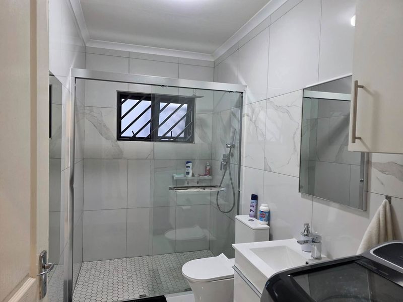 Modern bathroom featuring a walk-in shower with glass enclosure, wall-mounted vanity, and contemporary marble-look wall tiling.