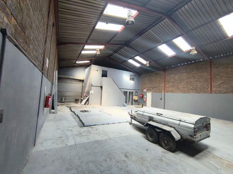 Spacious industrial warehouse unit featuring high ceilings with skylights, exposed brick walls, a roller shutter door, and a mezzanine level for additional storage or office space.