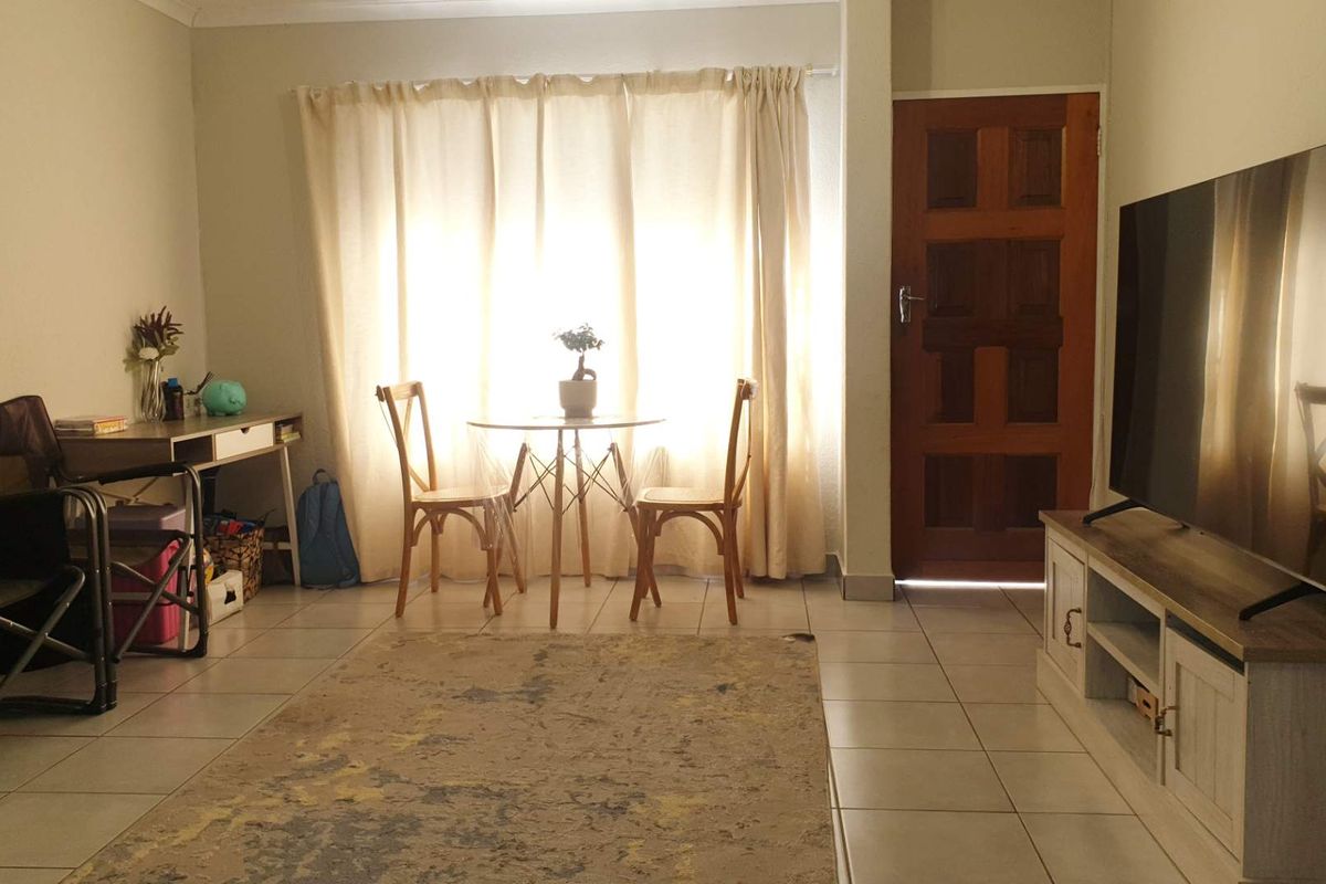 A living room area featuring tiled flooring and a wooden entrance door, providing a functional space with natural light from the window.