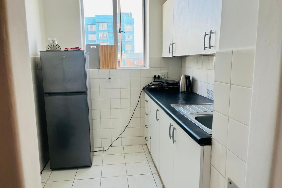 Compact kitchen featuring white cabinetry, dark laminate countertops, tiled splashbacks, and tiled flooring, providing a functional and efficient workspace.