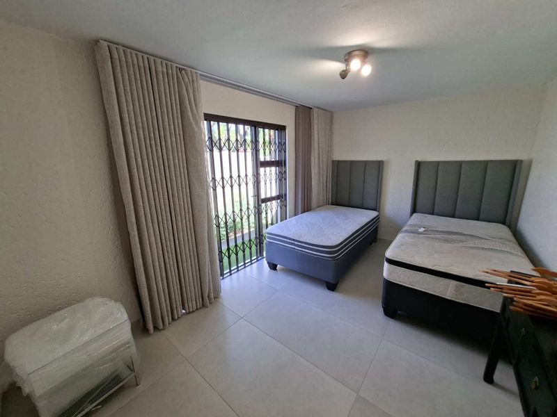 A bright bedroom featuring large format floor tiles, a sliding glass door with security gate, and neutral wall finishes.
