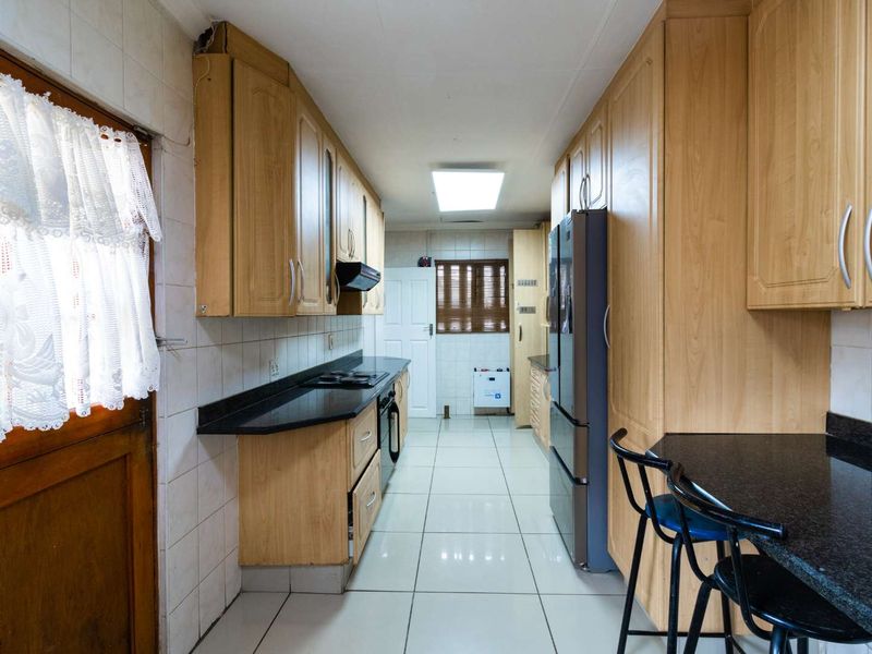 A functional galley-style kitchen featuring light wood cabinetry, dark granite countertops, built-in cooking appliances, and tiled flooring throughout.