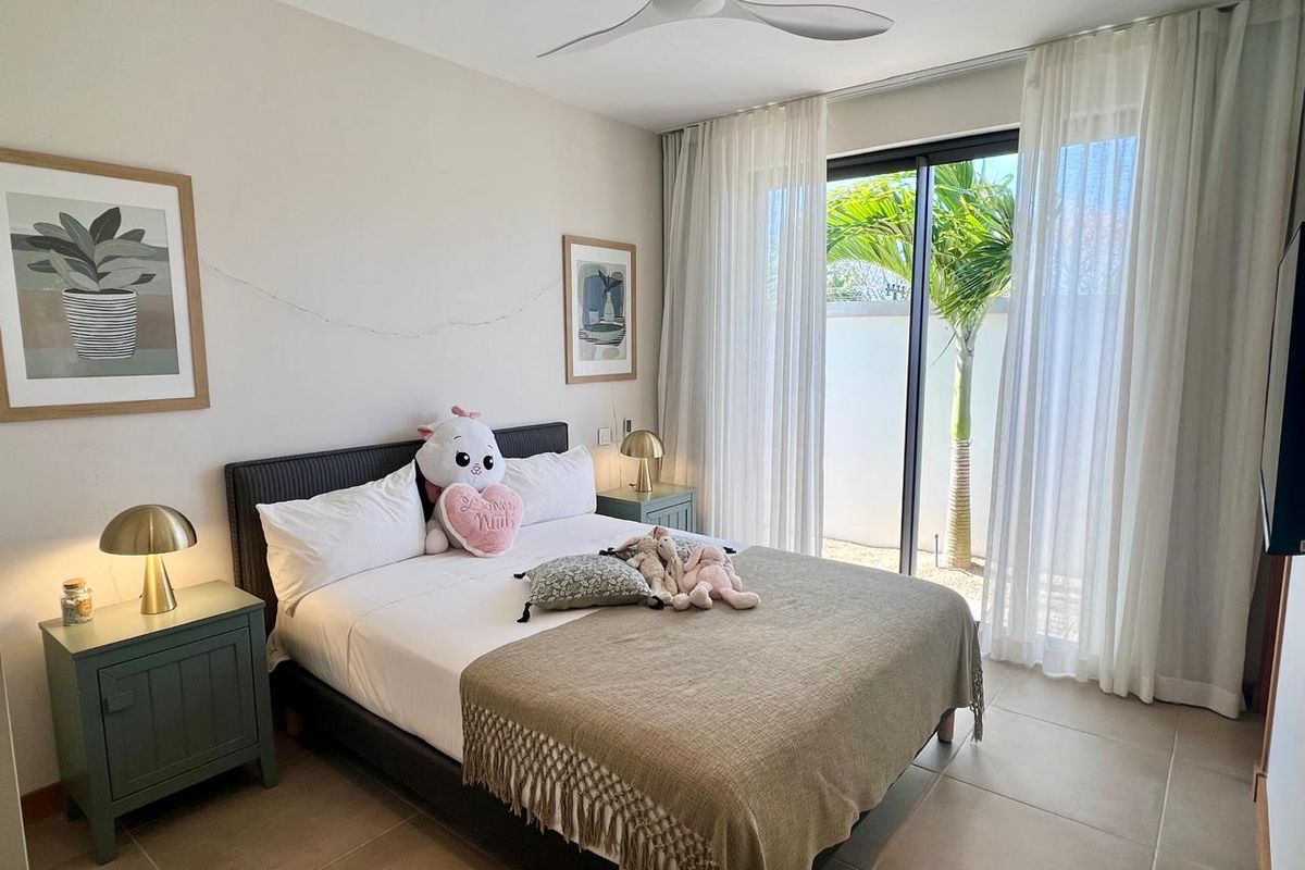 A well-maintained bedroom featuring large sliding glass doors that open to a private outdoor area, tiled flooring, and a modern ceiling fan.
