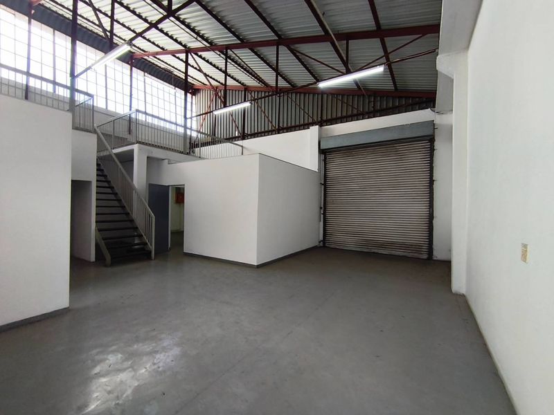 Spacious industrial warehouse unit featuring a high-clearance roof, mezzanine level with staircase access, and a large roller shutter door for easy loading.