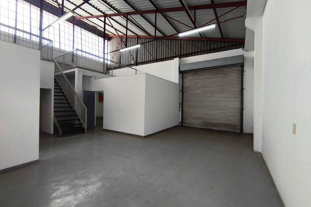 Spacious industrial warehouse unit featuring a high-clearance roof, mezzanine level with staircase access, and a large roller shutter door for easy loading.