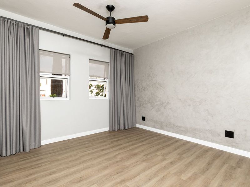 A bright, empty bedroom featuring modern laminate flooring, a textured feature wall, built-in cupboards, and a ceiling fan.