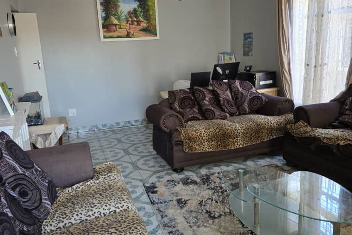 A living room featuring tiled flooring, a ceiling fan, and natural light from a window with curtains.