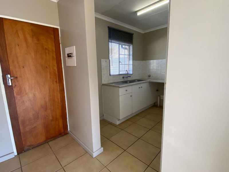 A compact, empty kitchen featuring built-in cabinetry, a double bowl sink, and tiled splashbacks, offering a functional space ready for modernization.