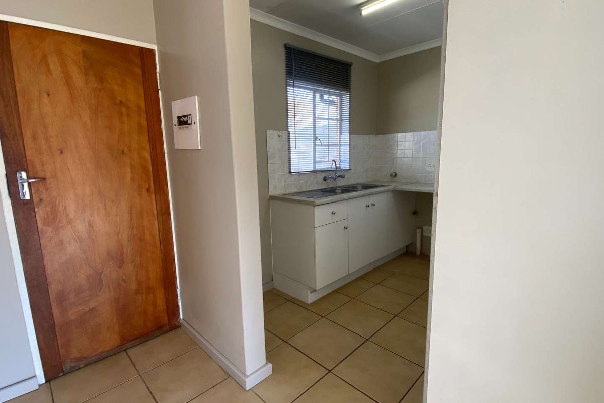 A compact, empty kitchen featuring built-in cabinetry, a double bowl sink, and tiled splashbacks, offering a functional space ready for modernization.