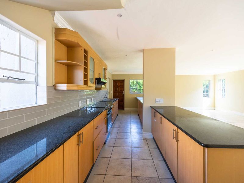 Spacious open-plan kitchen featuring light wood cabinetry, dark granite countertops, and a tiled backsplash, flowing seamlessly into the adjacent living area.