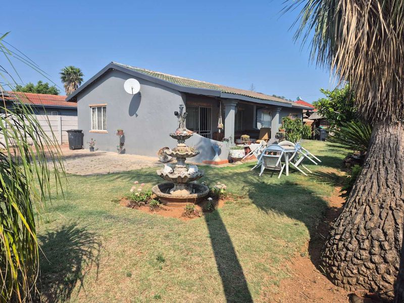 Rear view of the house featuring a paved patio area, a central garden fountain, and a surrounding lawn with boundary walling.