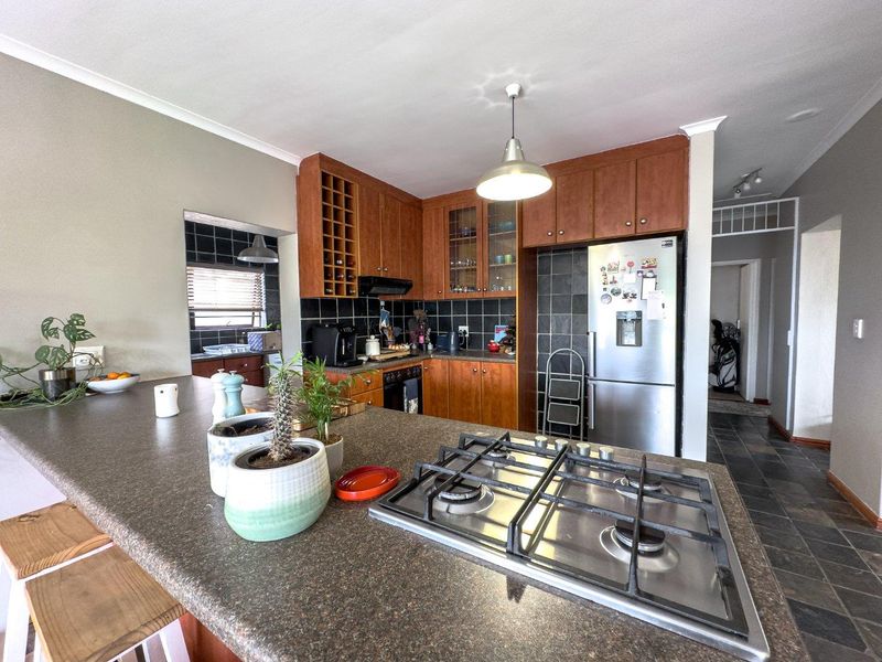 Functional kitchen featuring a central island with a built-in gas hob, dark stone countertops, wooden cabinetry, and a tiled backsplash.