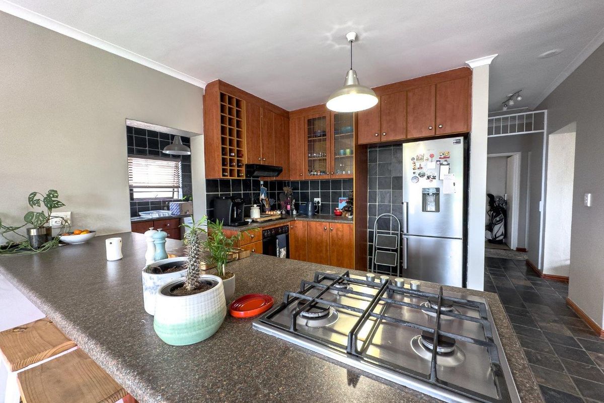 Functional kitchen featuring a central island with a built-in gas hob, dark stone countertops, wooden cabinetry, and a tiled backsplash.