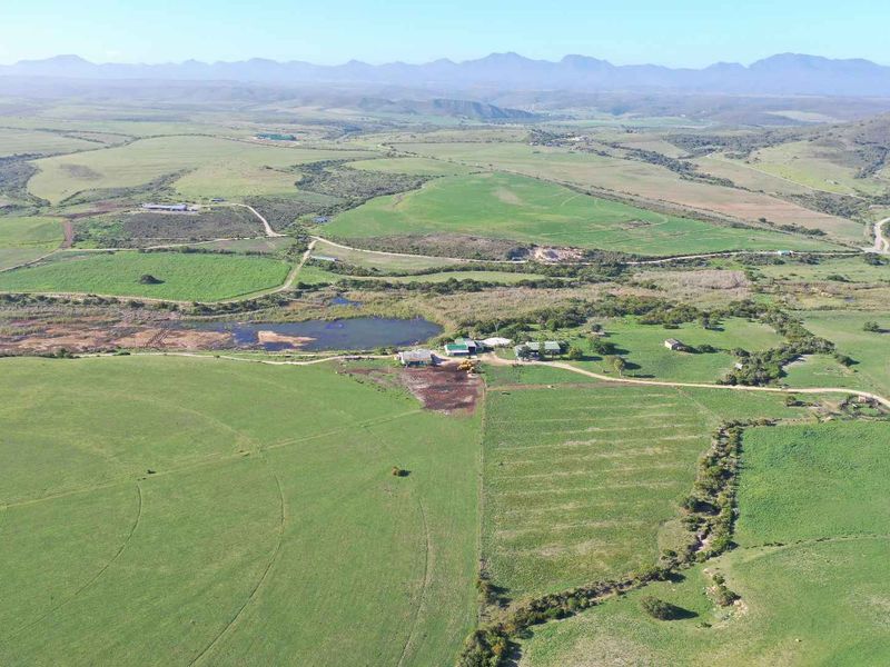 An aerial view of a large farm property featuring expansive green fields, irrigation infrastructure, a central dam, and various farm buildings.