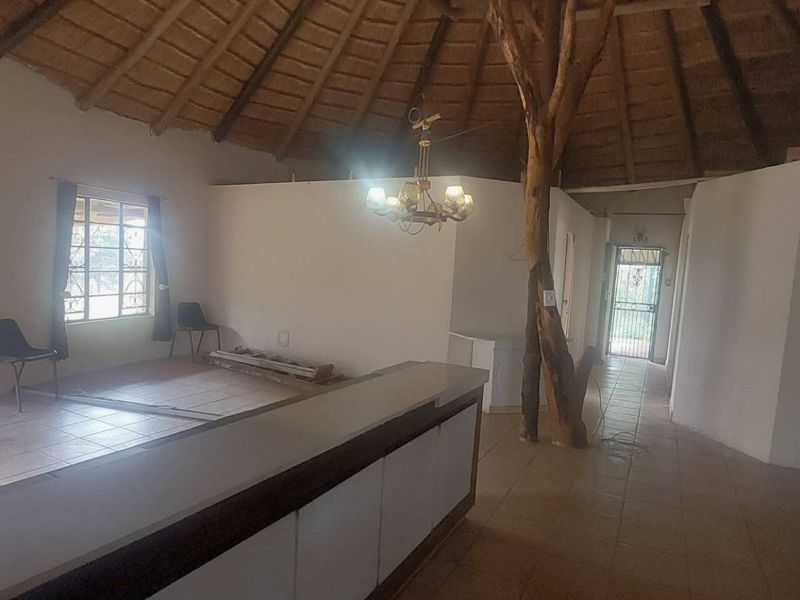 Open-plan living area featuring a traditional thatched roof, exposed timber support, and tiled flooring with direct access to the exterior.