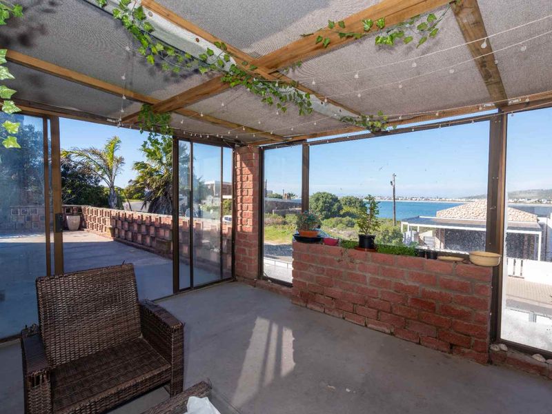 Covered patio area featuring exposed brick walls, sliding glass doors, and a timber-framed roof structure with scenic coastal views.