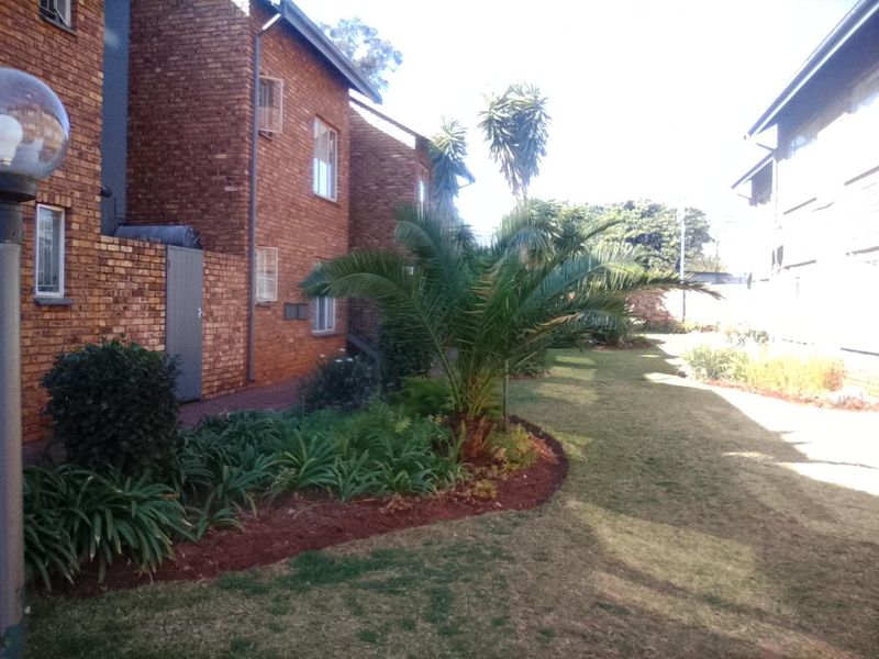 A view of the rear exterior of the apartment complex, featuring a well-maintained garden, lawn, and brick building facade.