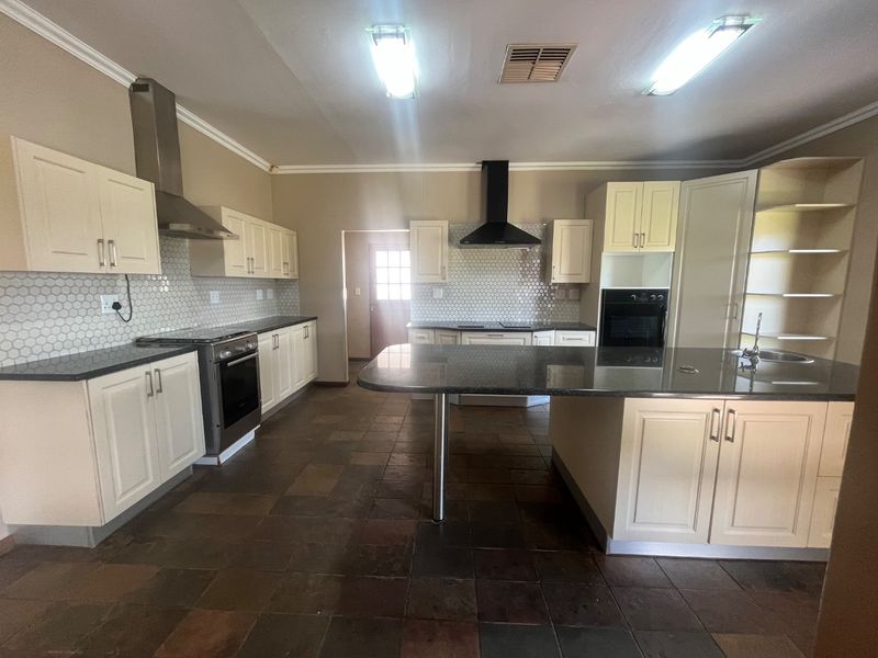 Spacious kitchen featuring cream cabinetry, granite countertops, a central island, and modern stainless steel appliances with a mosaic tile backsplash.