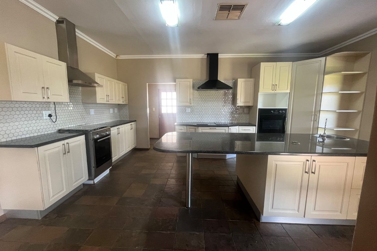 Spacious kitchen featuring cream cabinetry, granite countertops, a central island, and modern stainless steel appliances with a mosaic tile backsplash.