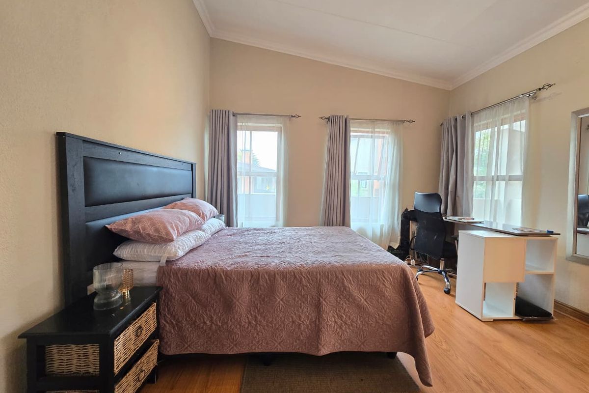 A well-lit bedroom featuring laminate flooring, coved ceilings, and multiple windows with installed curtain rods, providing a comfortable and functional living space.