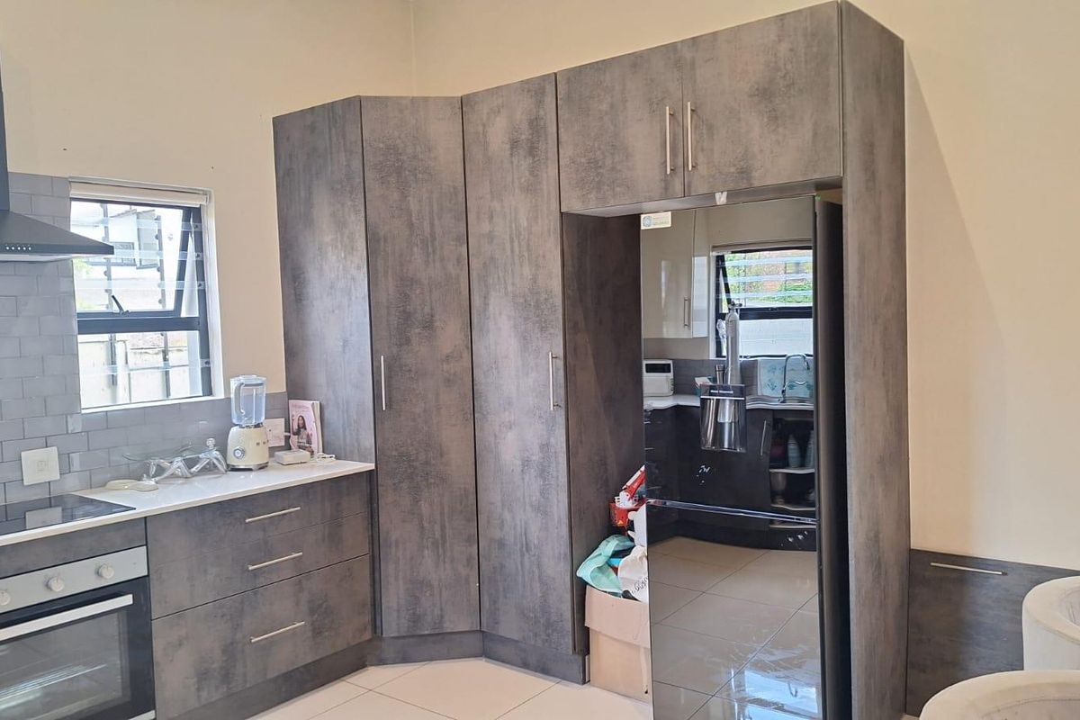 Modern kitchen featuring dark textured cabinetry, built-in oven, extractor fan, and a subway tile backsplash with light-colored tiled flooring.