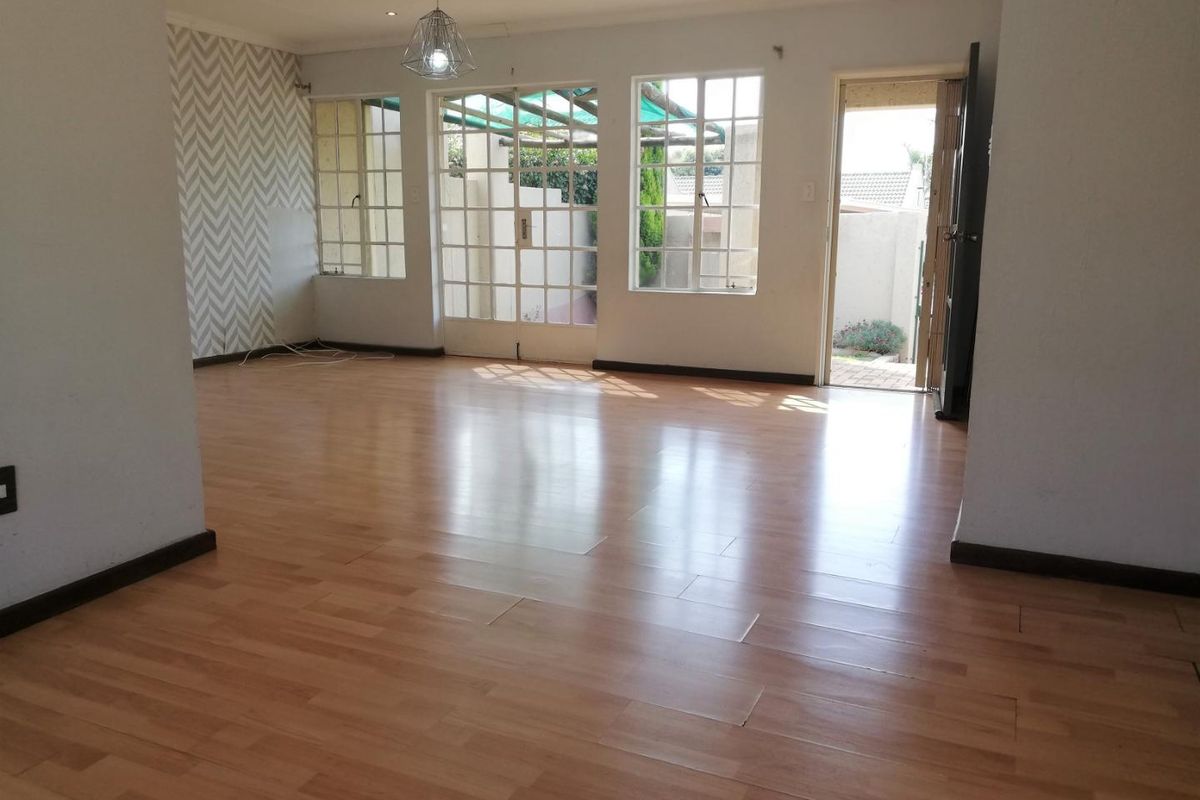 Spacious, empty living area featuring laminate flooring, recessed lighting, and direct access to the rear patio through glass-paned french doors.