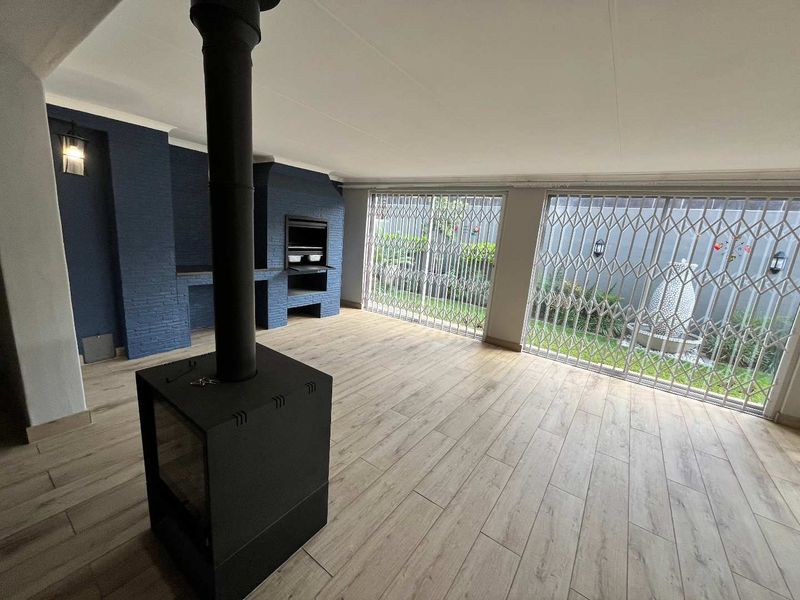 Spacious covered patio featuring a built-in braai, a modern freestanding fireplace, and large security-gated glass doors opening to the garden.