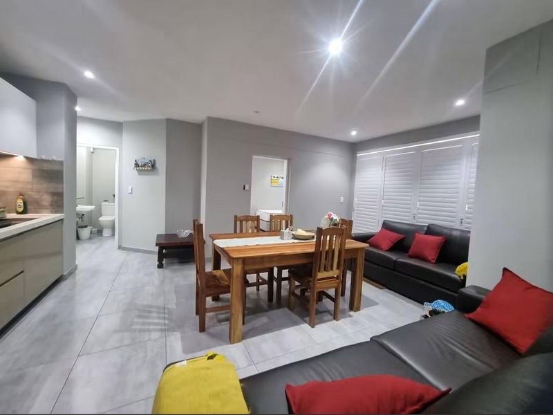 Spacious open-plan living and dining area featuring modern tiled flooring, recessed lighting, and plantation shutters, seamlessly connected to a contemporary kitchen.