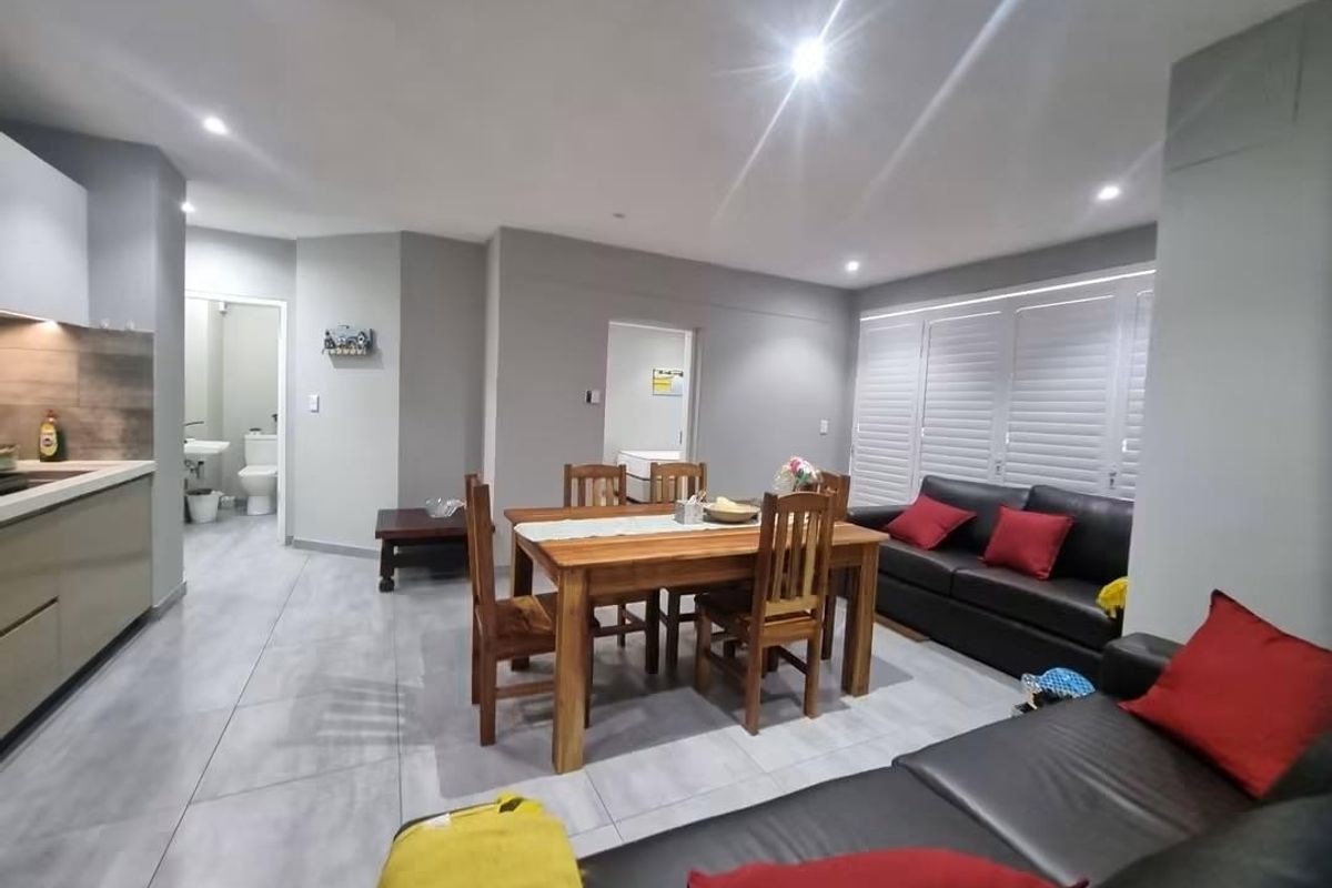 Spacious open-plan living and dining area featuring modern tiled flooring, recessed lighting, and plantation shutters, seamlessly connected to a contemporary kitchen.