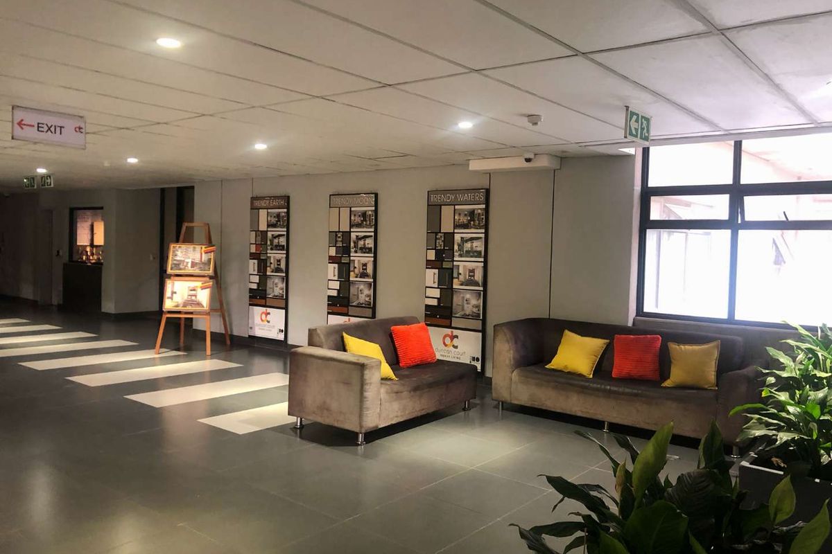 A spacious, well-lit apartment building lobby or hallway featuring tiled flooring, recessed ceiling lighting, and large windows providing natural light.