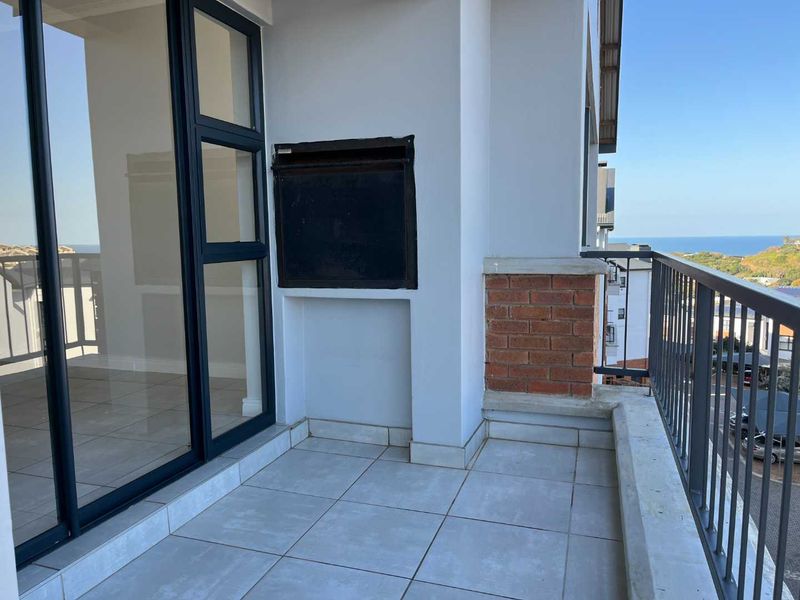 A spacious balcony featuring tiled flooring, a built-in braai, and a metal balustrade, offering an outdoor entertainment area with coastal views.