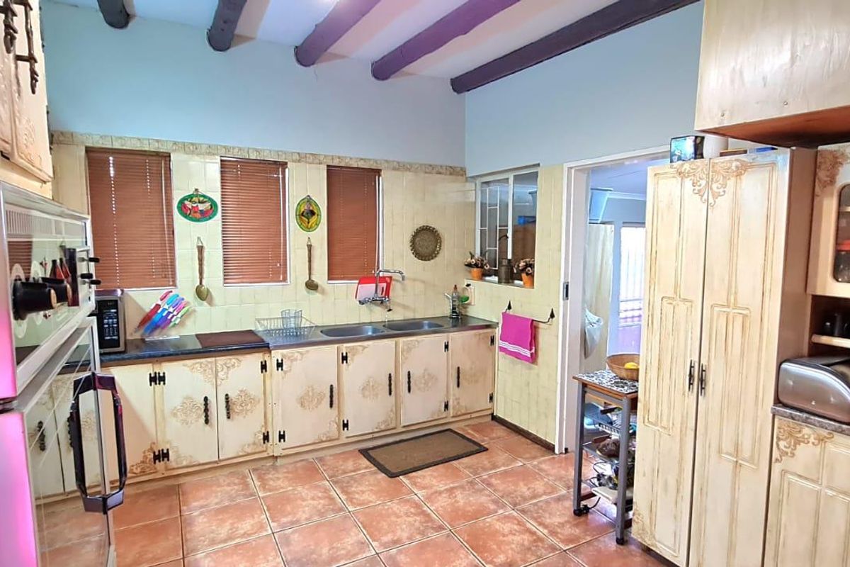 A functional kitchen featuring dated cabinetry, double basin sink, exposed ceiling beams, and tiled flooring, offering potential for a modern renovation.
