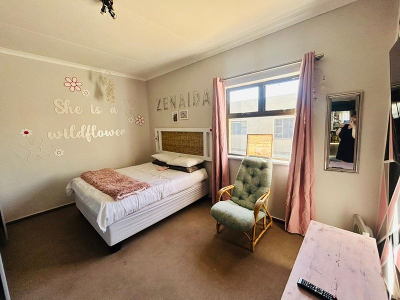 A functional bedroom featuring carpeted flooring, neutral wall finishes, and an aluminium-framed window providing natural light.