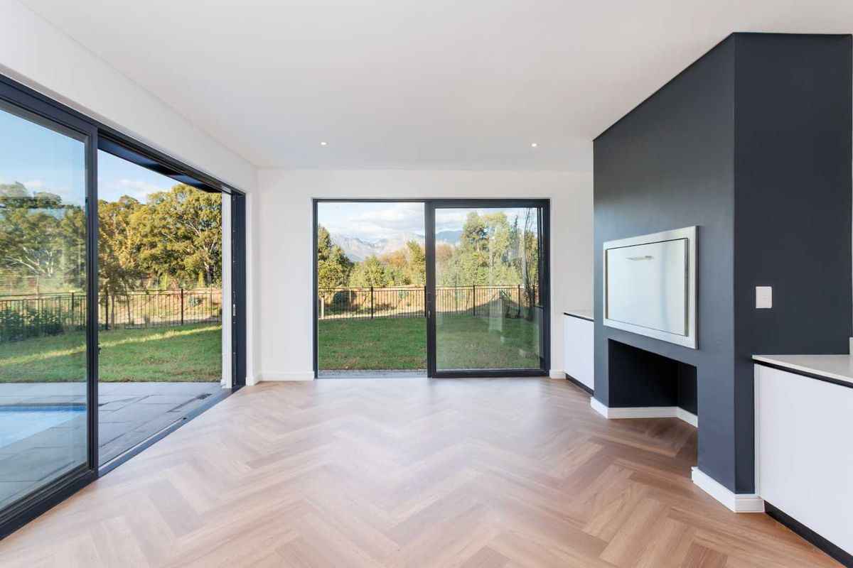 Modern open-plan living area featuring high-quality herringbone timber flooring, a built-in braai, and expansive sliding glass doors opening to the garden and pool area.