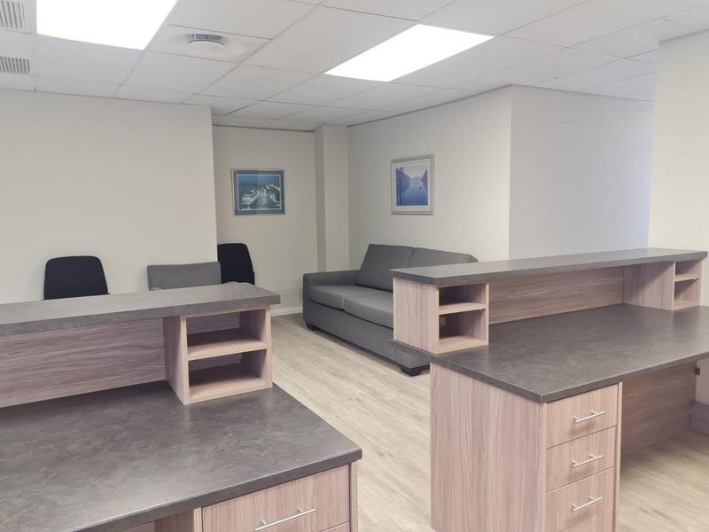A professional office space featuring built-in reception desks, modern laminate flooring, and a suspended ceiling with recessed lighting.