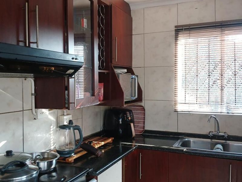 A functional kitchen featuring dark wood cabinetry, granite countertops, a stainless steel sink, and a tiled backsplash with an integrated extractor fan.