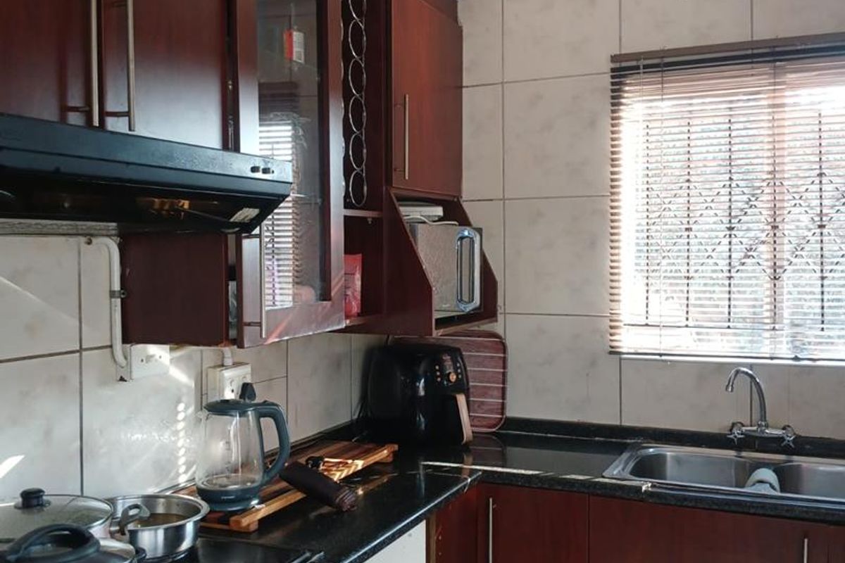 A functional kitchen featuring dark wood cabinetry, granite countertops, a stainless steel sink, and a tiled backsplash with an integrated extractor fan.