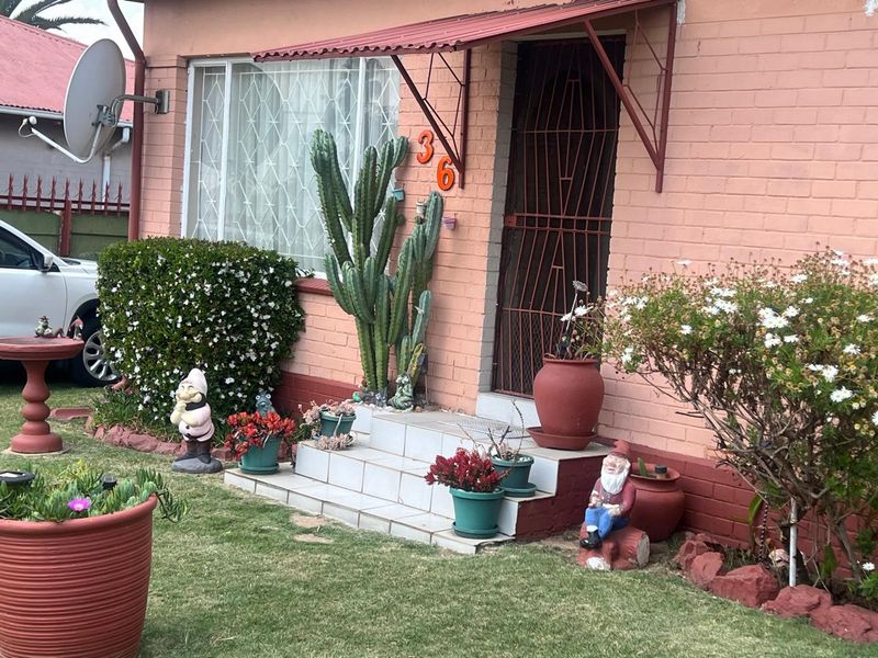 Front entrance of a brick house featuring a metal security gate, tiled steps, and a protective metal awning.