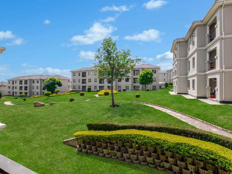 A well-maintained communal garden area featuring manicured lawns, paved pathways, and retaining walls between apartment blocks.