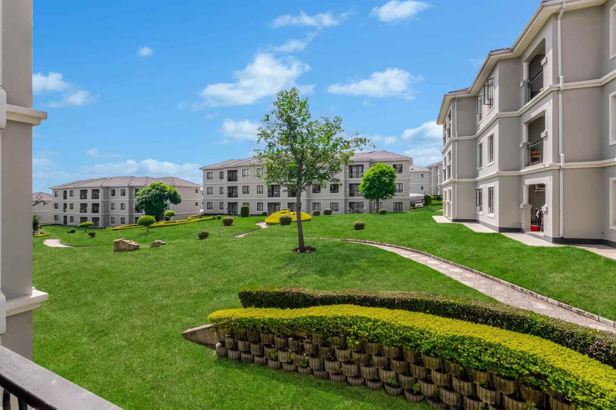A well-maintained communal garden area featuring manicured lawns, paved pathways, and retaining walls between apartment blocks.