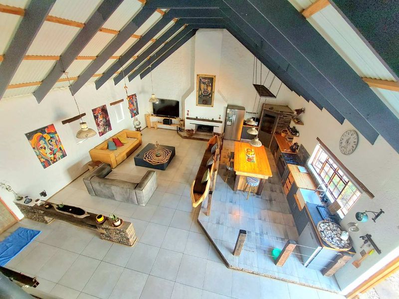 Spacious open-plan living area featuring a high vaulted ceiling with exposed beams, a central fireplace, and a functional kitchen with a large island.