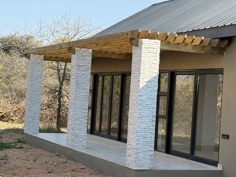 A modern covered patio featuring a timber pergola, stone-clad pillars, and large sliding glass doors providing seamless indoor-outdoor flow.