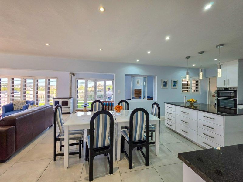 Spacious open-plan living and dining area featuring modern kitchen cabinetry, granite countertops, built-in oven, tiled floors, and a cozy wood-burning fireplace.