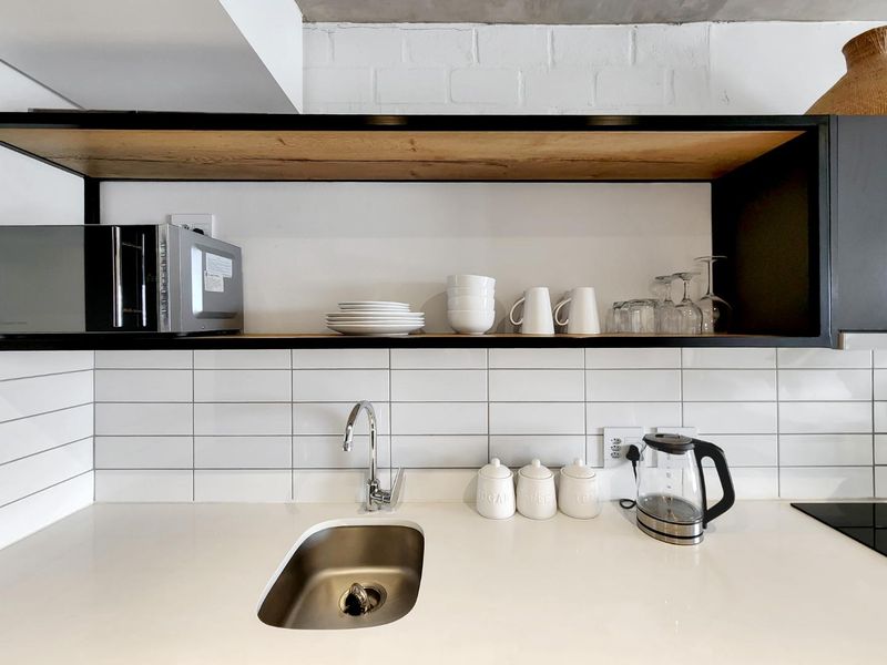 Modern kitchen area featuring a clean subway tile backsplash, sleek quartz countertops, an undermount sink, and stylish open shelving against an exposed brick wall.