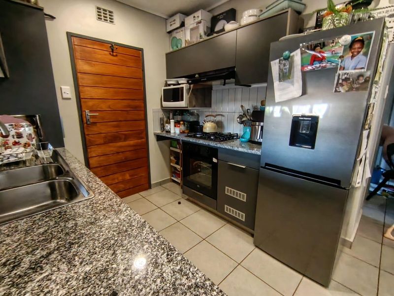 A functional kitchen featuring granite countertops, a double stainless steel sink, built-in oven with gas hob, and ample cabinetry with a tiled backsplash.