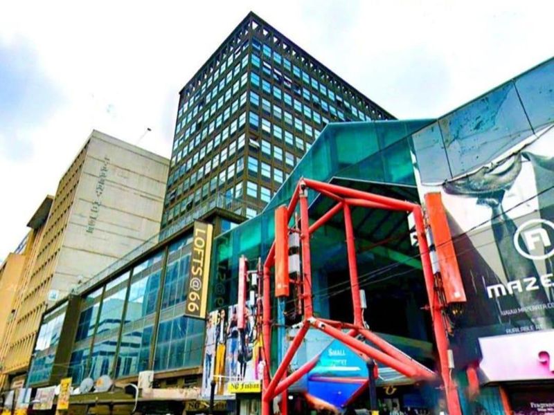 Exterior view of the Lofts@66 apartment building featuring a modern glass facade and prominent street-level commercial signage in a busy urban setting.